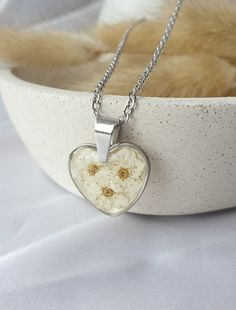 Heart shaped necklace, a harmonious blend of elegance and nature's beauty. Adorned with delicate dry spiraea flowers. The shimmering background adds a touch of radiance to the design, creating a captivating play of light that enhances the intricate detailing. Crafted from high-quality stainless steel, this piece exudes durability and longevity, ensuring it remains a cherished accessory for years to come. Nature-inspired Silver Heart Necklace, White Heart Pendant Necklace As Gift For Her, White Pendant Necklaces For Mother's Day, White Pendant Necklace For Mother's Day, Mother's Day Flower Shaped Jewelry With Heart Charm, Mother's Day Jewelry With Heart Charm And Flower Shape, Mother's Day Flower Jewelry With Heart Charm, Nickel-free White Gold Necklaces As A Gift For Her, Stainless Steel Heart Charm Jewelry As Gift For Her