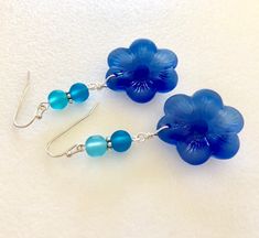 "Beautiful light sapphire blue or royal blue sea glass flowers are the feature of these pretty dangle earrings. Large 1\" sea glass flower is accented with contrasting shades of royal blue, teal and aqua blue sea glass rounds. Earrings are made of cultured tumbled sea glass and wire wrapped in German silver plated jeweler's wire. They hang from silver plated ear wires. Light sapphire blue earrings measure 2\" long and royal blue are 2 1/4\" long. Also available in Sterling silver. Listing is for Blue Flower Charm Drop Earrings, Elegant Blue Resin Earrings, Blue Sea Glass Dangle Jewelry, Blue Sea Glass Nickel Free Earrings, Blue Sea Glass Nickel-free Earrings, Nickel-free Blue Sea Glass Earrings, Blue Flower-shaped Jewelry For The Beach, Blue Flower Jewelry For The Beach, Blue Flower Earrings Nickel Free