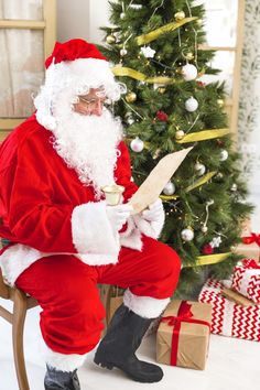 a man dressed as santa claus sitting in front of a christmas tree reading a book