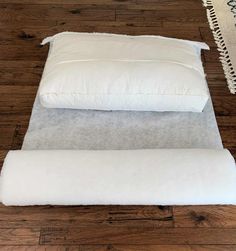 two white pillows sitting on top of each other in front of a rug and wooden floor