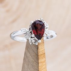 a ring with a garnet stone on top of a piece of wood in front of a wooden stand