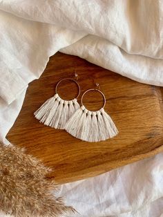 a pair of white tasselled hoop earrings sitting on top of a wooden table