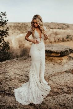 a woman standing on top of a rocky hillside wearing a wedding dress with an open back