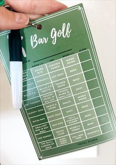 a person holding up a green bar golf score card with a pen in it's hand