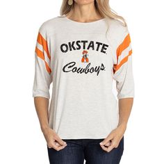 Elevate the style of your game day tee with this Oklahoma State Cowboys Sabrina Jersey T-shirt. It features the team name and logo accentuated by contrast-color side stitching and sleeve stripes. A rounded hem gives this Oklahoma State Cowboys shirt a more comfortable fit and feel. Collegiate Logo Print Tops For College, Varsity Tops With Team Name For Fan Gear, Game Day Football Season Tops With Logo Print, Football Season Game Day Logo Print Tops, Collegiate Team-colored Tops With Team Logo, Collegiate Game Day T-shirt With Team Name, Collegiate Athletic Heather Tops For Game Day, Varsity Logo Print Tops For College, College Football Season Tops With Text Print