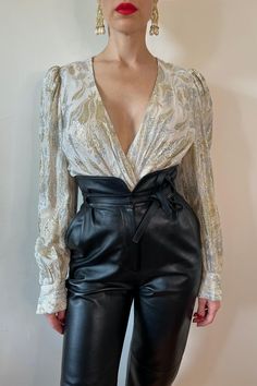 It's all couture and all mystery for the woman wearing this soft seducing silver and pearlescent wrap blouse. For maximum luxury; style with minimal makeup, a trademark red lip, and our Museum by Miss Gray couture Legacy Leather Pant. Fabric: Rayon, metallic Colour: Ivory, silver, gold Measurements: Chest 40", Waist 27", Length 21" Garment Care: Dry clean only Model: Height 5'7" - Chest 34", Waist 25", Hip 36.5" ⚜️⚜️⚜️ 10% surcharge on Etsy compared to our website due to fees 20% OFF at missgray Glamorous Formal V-neck Blouse, Glamorous V-neck Blouse, Elegant Gold Formal Tops, Elegant Gold Tops For Formal Occasions, Vintage V-neck Party Blouse, Vintage V-neck Blouse For Party, Elegant V-neck Blouse For Party Season, Glamorous V-neck Formal Blouse, Glamorous V-neck Blouse For Formal Occasions