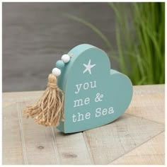 a wooden heart shaped box with tassels on it and the words you me & the sea written in white