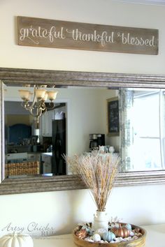 a mirror that is on the wall above a bowl with some flowers and eggs in it