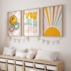 three framed pictures hang on the wall above a bench with pillows and storage bins