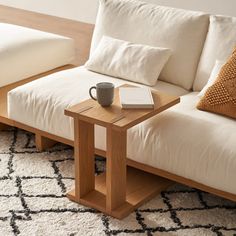 a wooden table with a book and cup on it in front of a white couch