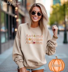 Get cozy in our Gildan 18000 sweatshirt, featuring a unique fall-themed design! The word 'Autumn' is repeated three times in vibrant orange, each word creatively incorporating a seasonal icon--a leaf, a scarecrow, and a pumpkin--into the lettering. This soft, durable sweatshirt is perfect for layering as the temperatures drop. Show off your love for the autumn season with this eye-catching, comfortable piece that celebrates all the best parts of fall." Ideal for any situation, a unisex heavy blend crewneck sweatshirt is pure comfort. These garments are made from polyester and cotton. This combination helps designs come out looking fresh and beautiful. The collar is ribbed knit, so it retains its shape even after washing. There are no itchy side seams on these sweaters.  .: Made with a medi Relaxed Fit T-shirt With Ribbed Cuffs For Fall, Trendy Graphic Print Sweatshirt For Fall, Fall Graphic Print Long Sleeve Sweatshirt, Orange Ribbed Cuffs Sweatshirt For Fall, Oversized T-shirt For Fall, Fall Graphic Print Crew Neck Hoodie, Fall Graphic Print Hoodie With Crew Neck, Trendy Orange Sweatshirt For Fall, Relaxed Fit Crew Neck Hoodie For Fall