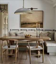 a dining room table with two chairs and a bench in front of it, next to a painting on the wall