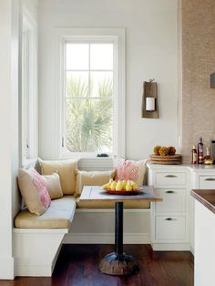 a window seat in a kitchen with fruit on the table and other items around it