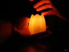 a person holding a lit candle in their hands with the light turned on and dark background