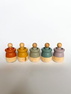 four small jars are lined up against a white background, each with a wooden top