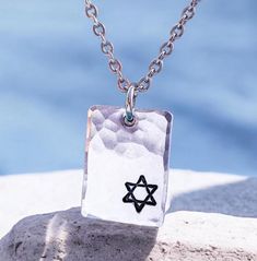 This necklace is sure to become a valued part of your own Judaica jewelry collection because of its unique combination of current elegance and traditional faith. Any friend of Israel and the symbols represented by this star would like to receive this necklace as a holiday gift! ➤FEATURES Pendant - 7/8'' x 5/8'' Choose chain ➤CHOOSE CHAIN 1. Dark metal - rolo chain - 2.4mm 2. Ball chain stainless steel - 2.4mm 3. Regular stainless steel chain - larger links  4. Regular stainless steel chain - smaller links 5. Ball chain - dainty ➤CHAIN LENGTHS Ball chains are 24 inches and can be shortened by snipping with scissors. Regular chains are 20 inches and can be ordered in other lengths.  Dark rolo chain is 20 inches ➤CRAFTSMANSHIP Everything Beautiful designs jewelry using only the highest qualit Spiritual Personalized Rectangular Jewelry, Personalized Rectangular Spiritual Necklace, Oxidized Finish Necklaces With Rectangular Pendant For Gift, Oxidized Rectangular Pendant Necklace For Gifts, Oxidized Finish Rectangular Pendant Necklace As Gift, Symbolic Star Of David Engraved Necklace, Engraved Sterling Silver Star Of David Necklace, Personalized Spiritual Necklace With Rectangular Pendant, Symbolic Necklace For Father's Day Gift