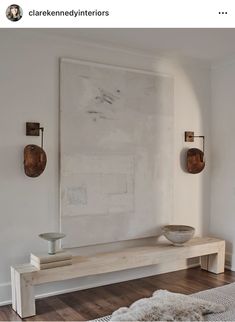 a large white painting hanging on the wall next to a wooden bench in a living room