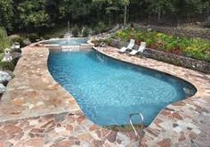 an empty swimming pool surrounded by stone steps and lawn chairs with trees in the background