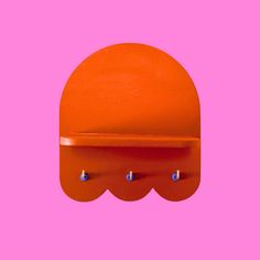 an orange shelf with two hooks on it against a bright pink background that has three small blue dots at the top