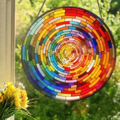 a stained glass sun catcher hanging on a window sill with flowers in the foreground