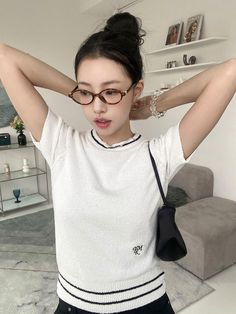 a young woman wearing glasses and holding her hair in one hand while standing next to a couch