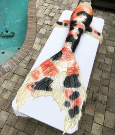 an artisticly painted fish laying on top of a white towel next to a swimming pool