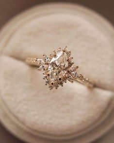 an engagement ring sitting on top of a white cloth covered box with a diamond in the center