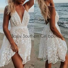 two women in white dresses are standing on the beach and one is touching her hair