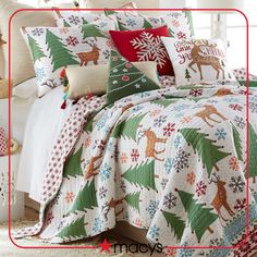 a bed covered in christmas themed pillows and blankets with deers, snowflakes and trees on them