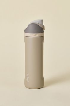 a gray and white blender bottle sitting on top of a beige table next to a wall