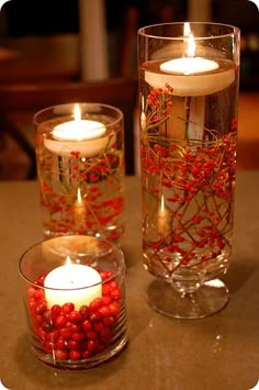 two glass vases filled with red berries and candles