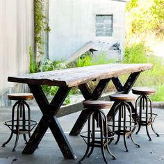 an outdoor table with four stools and a bench in front of a building that has vines growing on it