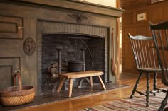 an old fashioned fireplace in a wood paneled living room with rocking chair and table