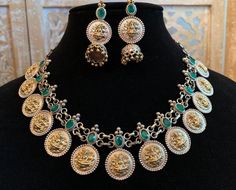 A really gorgeous jewelry set made from a mixture of pure brass (80%) and pure silver (20%). The design features small coin pine structures with Goddess Laxmi engraved on it neatly with a bright green stone on top of each coin. The earring is also same with a small jhumka added. The quality of the jewelry is top quality due to the use of authentic brass and silver. 100% guarantee on the gold and silver polish. Necklace is adjustable- loops in the back. Care Instruction: Avoid heat & substanc Dual-tone Temple Jewelry In Brass, Silver Brass Jewelry With Dual-tone, Dual-tone Brass Temple Jewelry, Silver Dual-tone Brass Jewelry, Elegant Gold Jewelry Sets With Oxidized Finish, Fusion Style Dual-tone Brass Jewelry, Fusion Dual-tone Brass Jewelry, Gold Jewelry With Oxidized Finish For Celebration, Silver Dual-tone Jewelry For Celebration