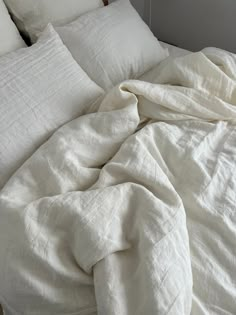 an unmade bed with white sheets and pillows