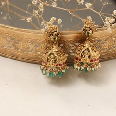 Description: These Nakshi jhumkas showcase the divine presence of Goddess Lakshmi, intricately designed with exquisite craftsmanship. A hint of color is added through the subtle jadau work on the rim, complemented by the delicate green beads that hang gracefully, adding a refined touch to the traditional design. These jhumkas effortlessly combine elegance and tradition, making them a standout accessory. Product Information: Materials used: 925 Silver with Antique Gold Plating Stones: High Grade Wedding Jhumkas With Intricate Design For Diwali, Chandbali Jhumkas With Intricate Design For Navratri, Navratri Chandbali Jhumkas With Intricate Design, Intricate Chandbali Jhumkas For Navratri, Temple Jewelry Style Round Jhumkas With Intricate Design, Temple Jewelry Jhumkas With Intricate Design For Diwali, Temple Jewelry Style Jhumkas With Intricate Design, Temple Jewelry Style Jhumkas For Wedding With Cutdana, Traditional Jhumkas With Intricate Design For Festivals