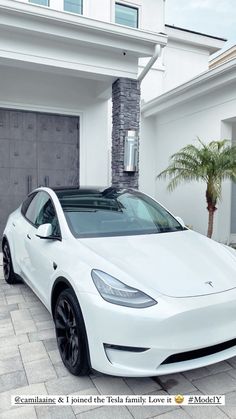 a white tesla model 3 parked in front of a house next to a palm tree