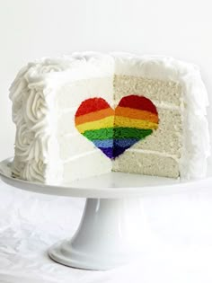 a white cake with a rainbow heart cut out of it's side on a plate