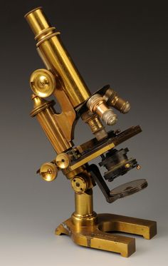 an antique brass microscope on a stand with the focus lens pointed up to it's side