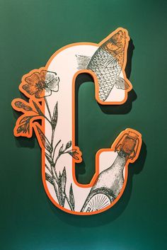 the letter c is decorated with flowers and fish on it's side, as well as an orange sticker