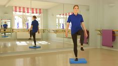 a woman is standing on a blue mat in front of a mirror and doing exercises