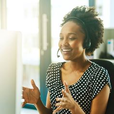 a woman wearing a headset sitting in front of a computer screen and talking on the phone