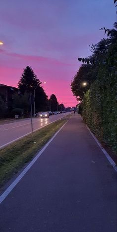 an empty street at dusk with the sun setting in the distance and cars driving down the road