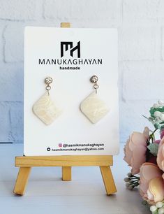 a pair of white earrings sitting on top of a wooden stand next to pink flowers