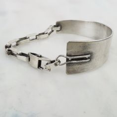 Mexican-born Los Angeles jeweler, Beth Orduna, made this unique asymmetrical sterling silver link bracelet. Half of the bracelet is constructed with thick 9mm by 5mm brushed silver links. The other half is a large 3 9/16-inch tapered silver form that wraps around the side of the wrist. The custom made lobster clasp has a wonderful machine age look to it and would look attractive worn at the top of the wrist or back side. The end link is signed, "Orduna" (attributed to Beth) and the bracelet tested as sterling silver purity. The bracelet has an approximate 6 1/2-inch inner circumference. This piece is in very good pre-owned condition with minor surface wear and patina.  Please see photos and detailed measurements below.  Total Wt: 19.5 grams Approx. Inner circumference: 6 1/2 inches Widest Modern Sterling Silver Bracelet With Hooks And Links, Modern Sterling Silver Bracelets With Hook And Links, Modern Sterling Silver Chain Bracelet, Modern Sterling Silver Bracelet With Rectangular Links, Modern Sterling Silver Chain Bracelet With Silver Clasp, Modern Silver Chain Bracelet With Sterling Clasp, Minimalist Sterling Silver Bracelet With Hooks And Links, Modern Link Chain Bracelet With Sterling Silver Clasp, Modern Silver Jewelry With Rectangular Links