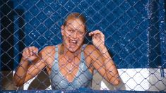 a woman is standing behind a chain link fence with her hands up in the air