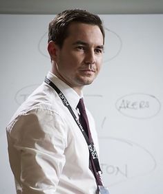 a man standing in front of a white board with writing on it and holding a tie around his neck