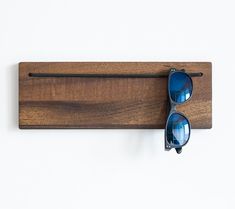 a pair of sunglasses hanging on a wooden wall mounted eyeglass holder with metal bar