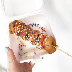 a person holding a donut with sprinkles on it in a plastic container