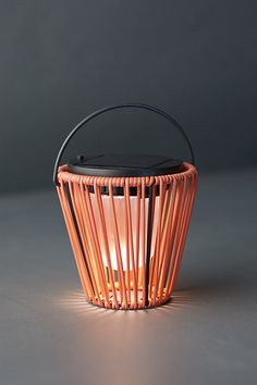 a light that is inside of a basket on a table with a black lid and handle